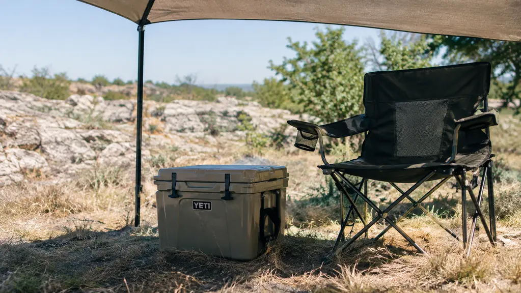 A cooler on the ground beside a camp chair under a shade canopy at midday