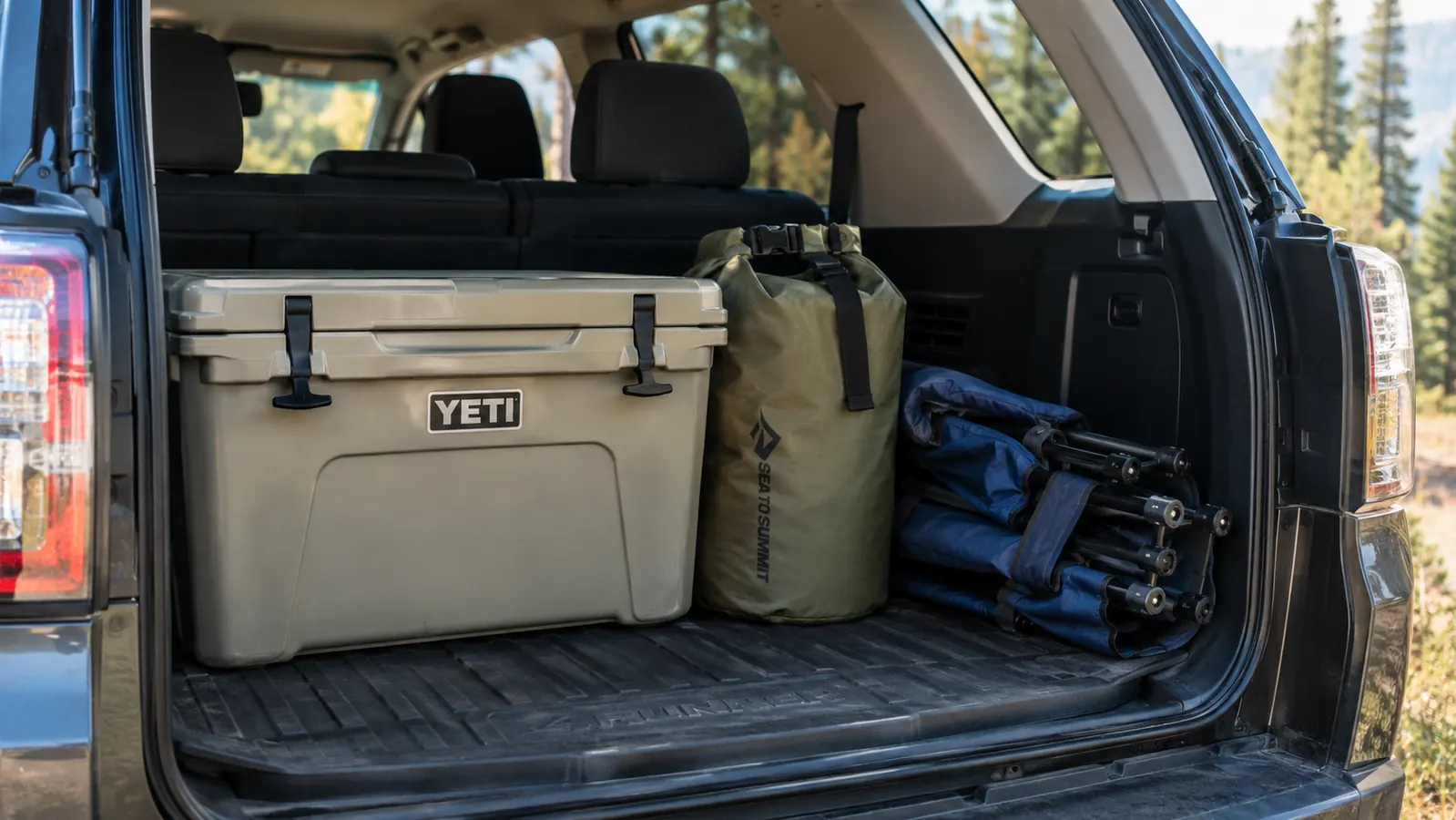 A cooler sitting in the cargo area of a 4Runner next to a dry bag and folded camp chairs